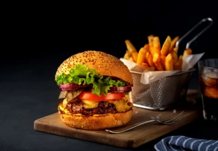 Cheeseburgare med sallad, tomat, och lök på sesamfröbröd, serverad med pommes frites och kall dryck, perfekt för måltid eller snabbmatkoncept.
