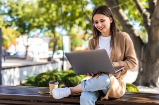 En kvinna med laptop jobbar utomhus i en park.